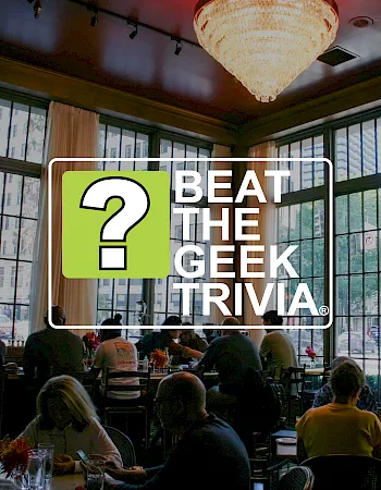 A restaurant meeting scene with a sign reading “BEAT THE GEEK,” featuring a big green question mark, in front of diners.
